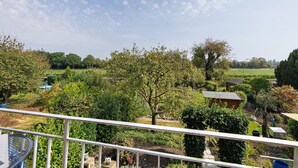 Blick in einen Garten von einem Balkon mit Metallgeländer, einschließlich eines kleinen Schuppens und verschiedener Bäume und Sträucher.