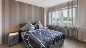 Ein Schlafzimmer mit Bett, Nachttischen, einem Fenster mit Jalousien und einer Heizung.