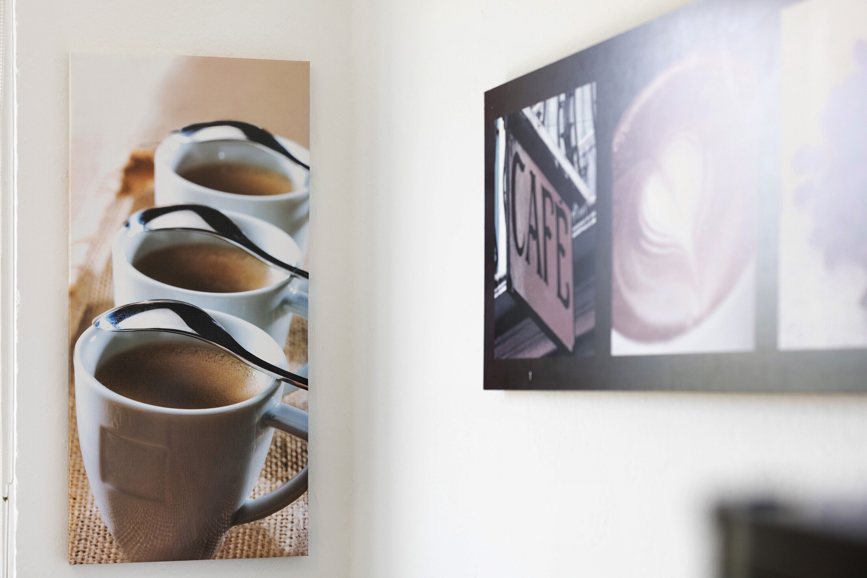 Una pared con un cuadro de cuatro tazas de café y un cuadro de un edificio con la palabra 'CAFE'.