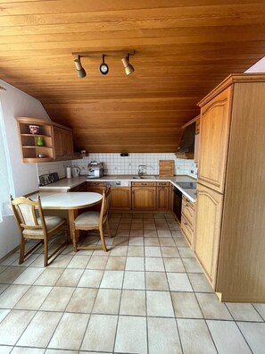 Une cuisine avec des meubles de rangement en bois, une table à manger avec des chaises et un sol carrelé.