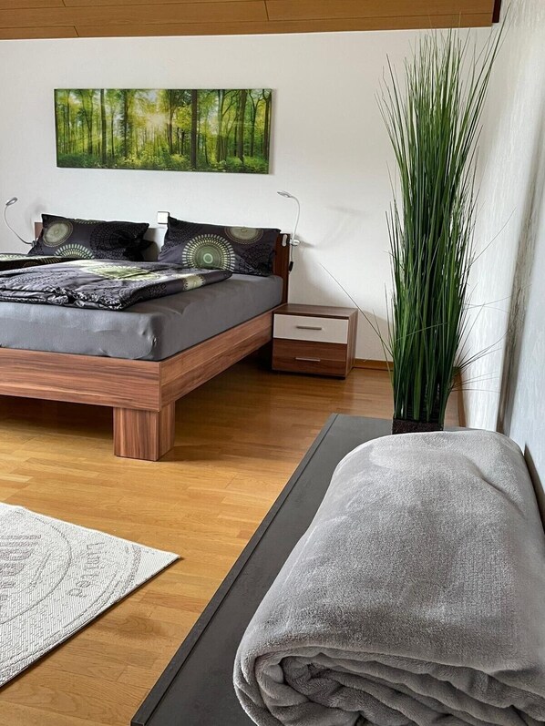 Une chambre  à coucher moderne avec un lit, une table de chevet, une lampe et une grande plante verte.