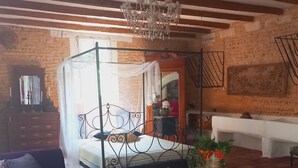 A bedroom with a four-poster bed, a wooden chest of drawers, a purple sofa, a red armchair, and a red carpet. - Mas Provençal à 10 Minutes de Nîmes. Animaux de Compagnie Acceptés ! (Générac)