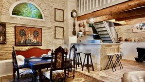 A rustic interior with a dining area featuring a wooden table and chairs, a bar area with stools, and a staircase leading to an upper level. - Mas Provençal à 10 Minutes de Nîmes. Animaux de Compagnie Acceptés ! (Générac)