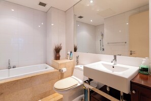 Un baño moderno con bañera, inodoro, lavamanos y un espejo grande.