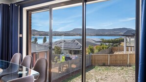 Een balkon met een glazen deur, een tafel met stoelen en uitzicht op een meer en huizen.