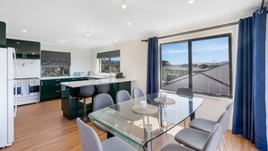 Een moderne keuken met een centraal eiland, een eetgedeelte met een glazen tafel en een groot raam voorzien van gordijnen.