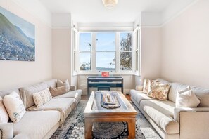 Sala de estar com dois sofás, uma mesa de centro e vista para uma montanha através de uma janela ampla.