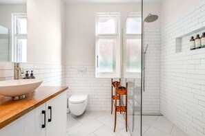 Features a sleek, white-tiled bathroom with a large vessel sink, glass-enclosed shower, and a toilet.
