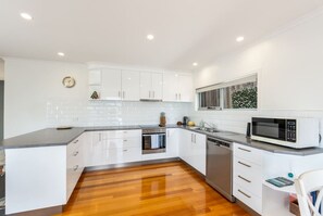 A modern kitchen with white cabinetry, a wooden floor, and a microwave.