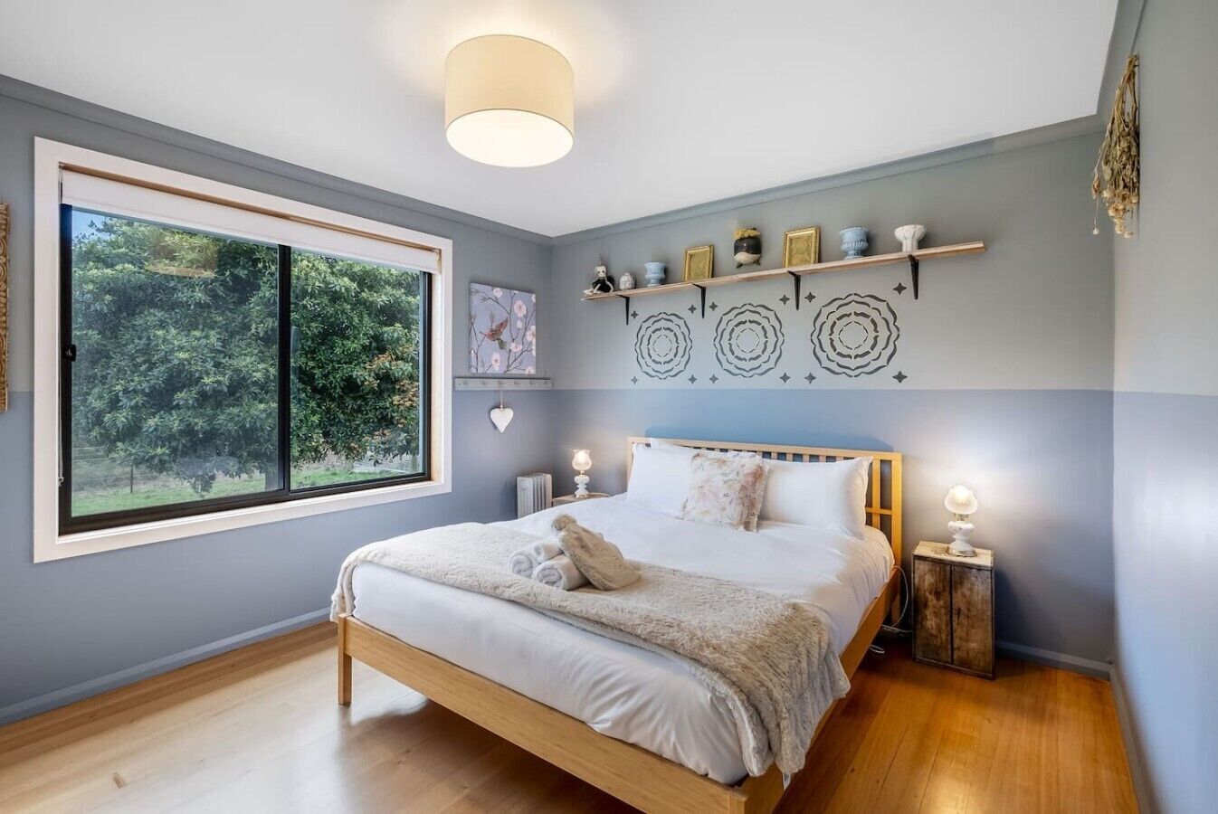 Un dormitorio con un ventanal grande, una cama, mesitas de noche y decoración mural.