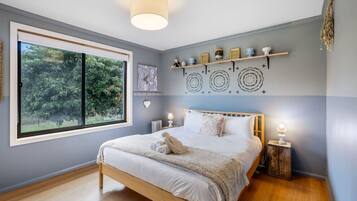 Un dormitorio con un ventanal grande, una cama, mesitas de noche y decoración mural.