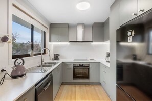 A compact kitchen with a dishwasher, oven, and stainless steel refrigerator. - Peaceful Beachside Home (Clifton Beach)