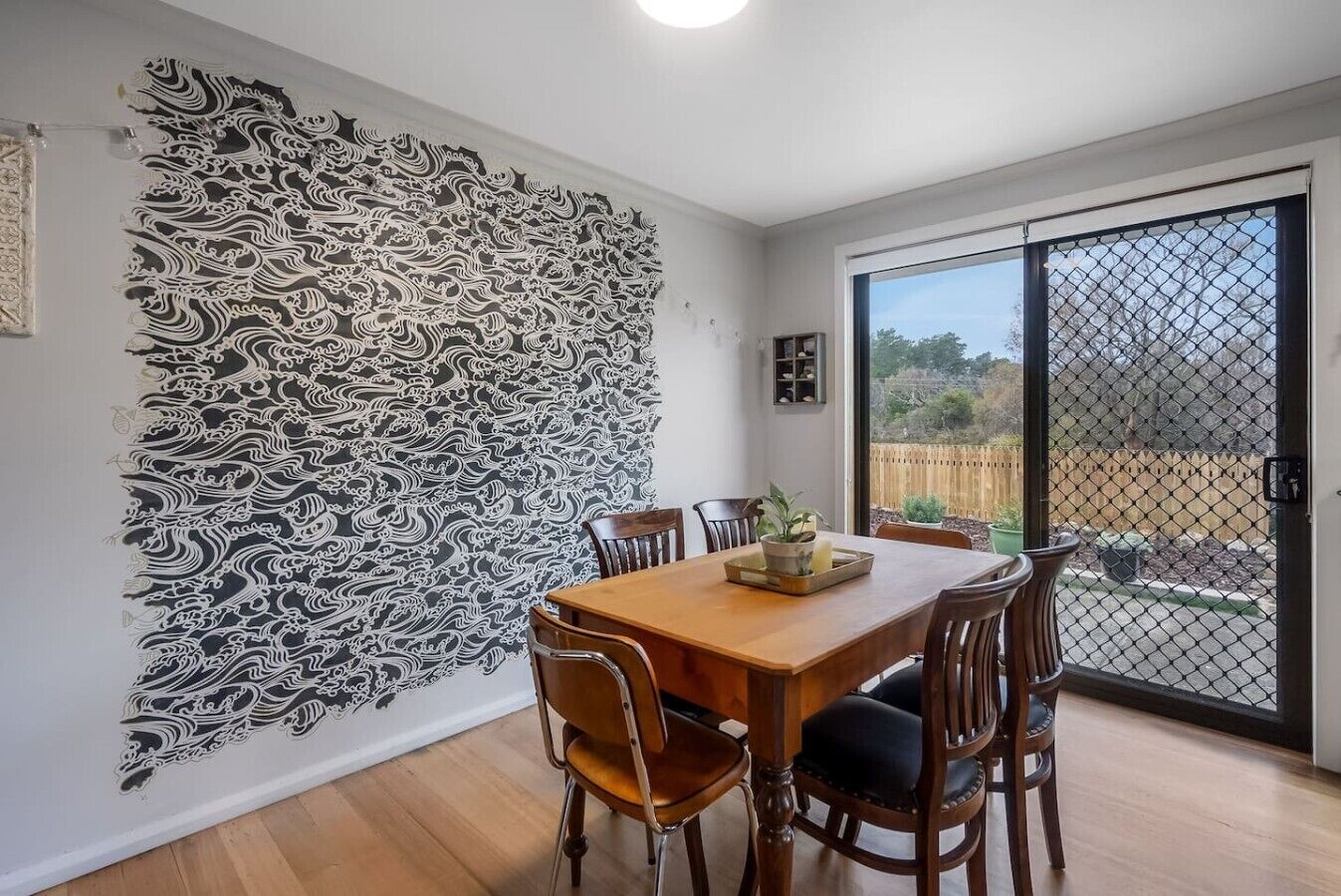 A dining area with a wooden table and chairs, a decorative wall with intricate patterns, and a view through a sliding glass door.