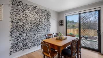 A dining area with a wooden table and chairs, a decorative wall with intricate patterns, and a view through a sliding glass door.