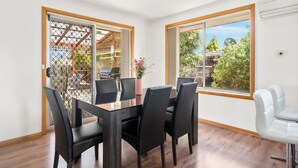 Zona pranzo con tavolo in legno e sedie nere, una porta scorrevole in vetro che dà su un patio esterno con una griglia, e un'ampia finestra vista alberi.