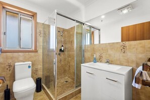 A modern bathroom with a glass-enclosed shower, a white toilet, and a vanity with a mirror.