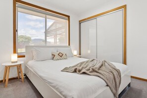 A bedroom with a bed, a bedside table, a lamp, a window, and a wardrobe.