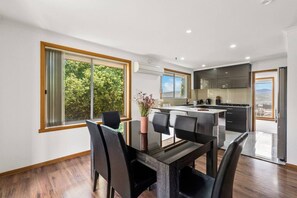 A modern kitchen with a dining area, large windows, and a view of greenery.