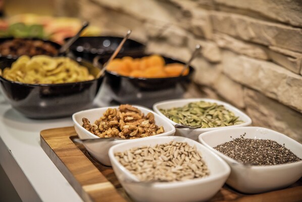 A buffet table with various food items in bowls, including nuts, seeds, and vegetables. - Hotel Brixen (Prague)