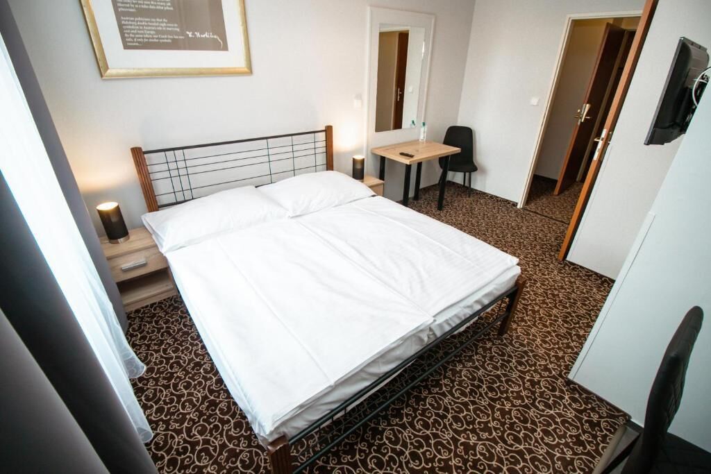 A hotel room with a bed, a desk, a chair, and a mirror.