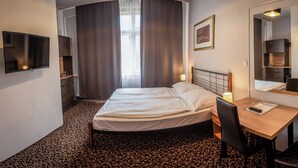 Una habitación de hotel con cama, escritorio, silla y televisión montada en la pared.