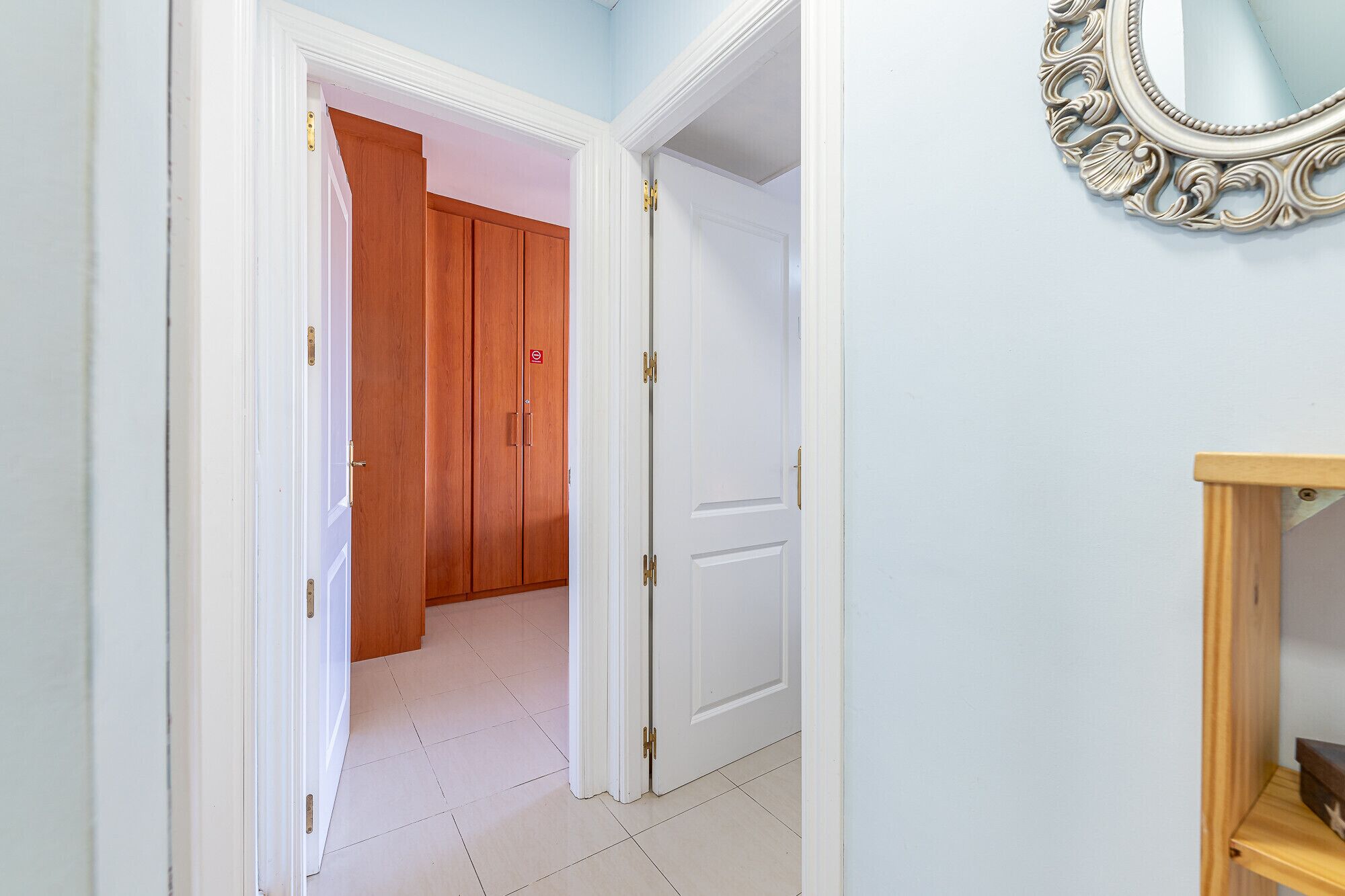 Un couloir avec une armoire en bois, une porte blanche et un miroir accroché au mur.