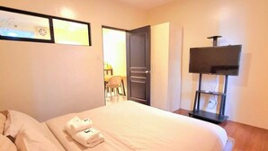 A hotel room with a bed, a TV on a stand, a door leading to a bathroom, and a small table with chairs.