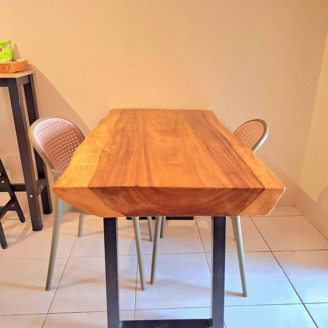Une table rectangulaire en bois, dotée de pieds en métal, accompagnée de deux chaises en osier.