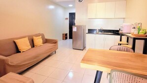 A compact living space with a sofa, a dining table, a refrigerator, and a kitchen area with cabinets and a sink.