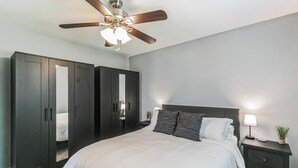 Quarto com cama, ventilador de teto, mesa de cabeceira e guarda-roupa.