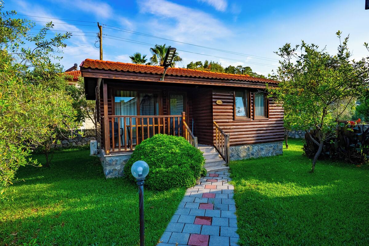 Een houten vakantiehuisje met een veranda, een pad van stenen en een verzorgd gazon.