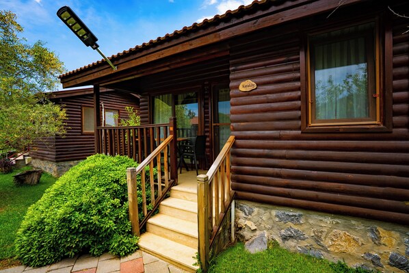 Une cabane en rondins avec un escalier en bois menant à une véranda, une enseigne indiquant « Kavakoy » et des fondations en pierre.