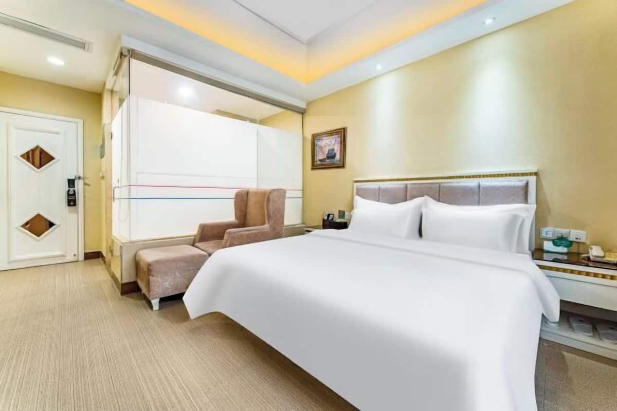 A hotel room with a large bed, a chair, a desk with a telephone, and a door with a small window.