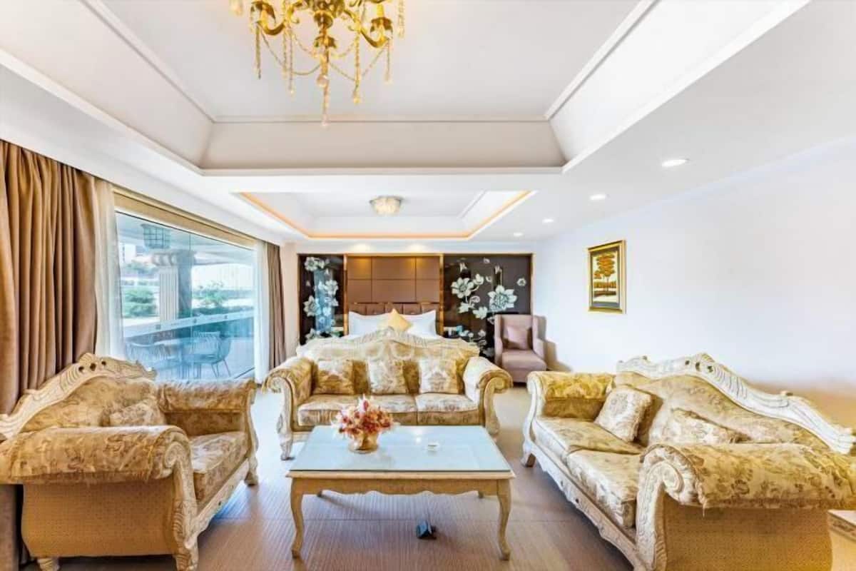 A luxurious living room with ornate sofas, a chandelier, and a large window offering a view.