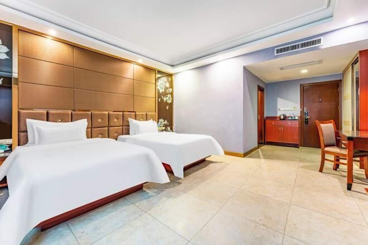 A hotel room with two beds, a wooden headboard, a small dining table, and a cabinet.