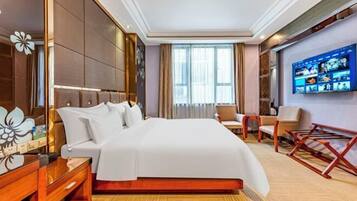 Una habitación de hotel con una cama grande, un televisor en la pared, un escritorio y una silla.