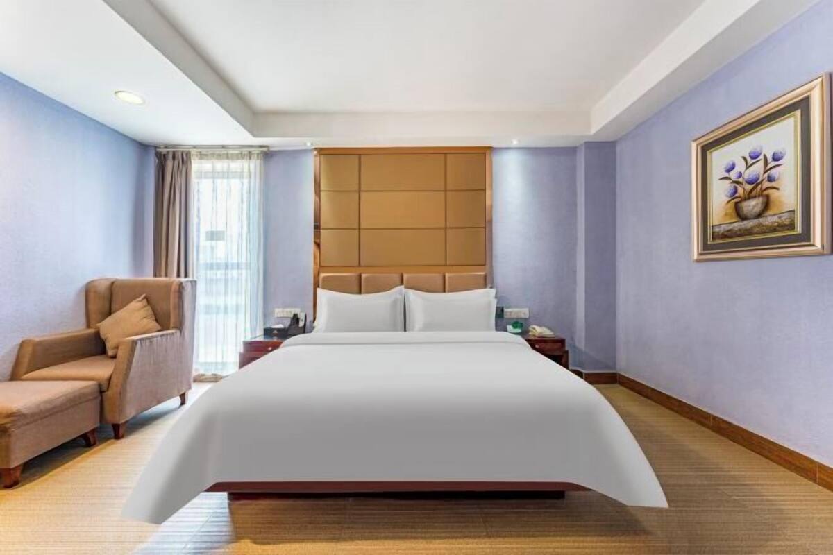 A hotel room with a large bed, a chair, a nightstand, and a painting on the wall.