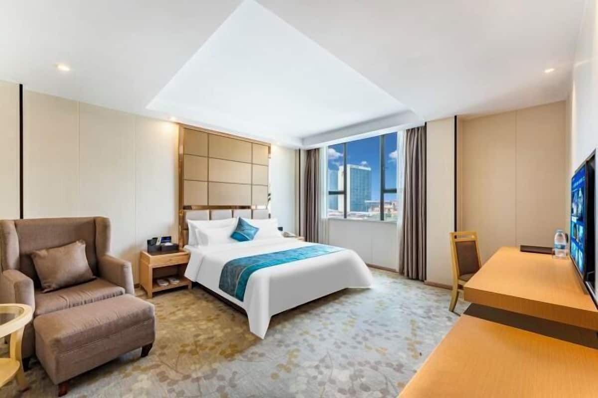 A hotel room with a bed, a sofa, a desk, and a TV.