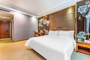 A hotel room with a large bed, a wooden nightstand, a desk with a chair, and a decorative wall panel. - Yuheng Hotel Foshan (Foshan)