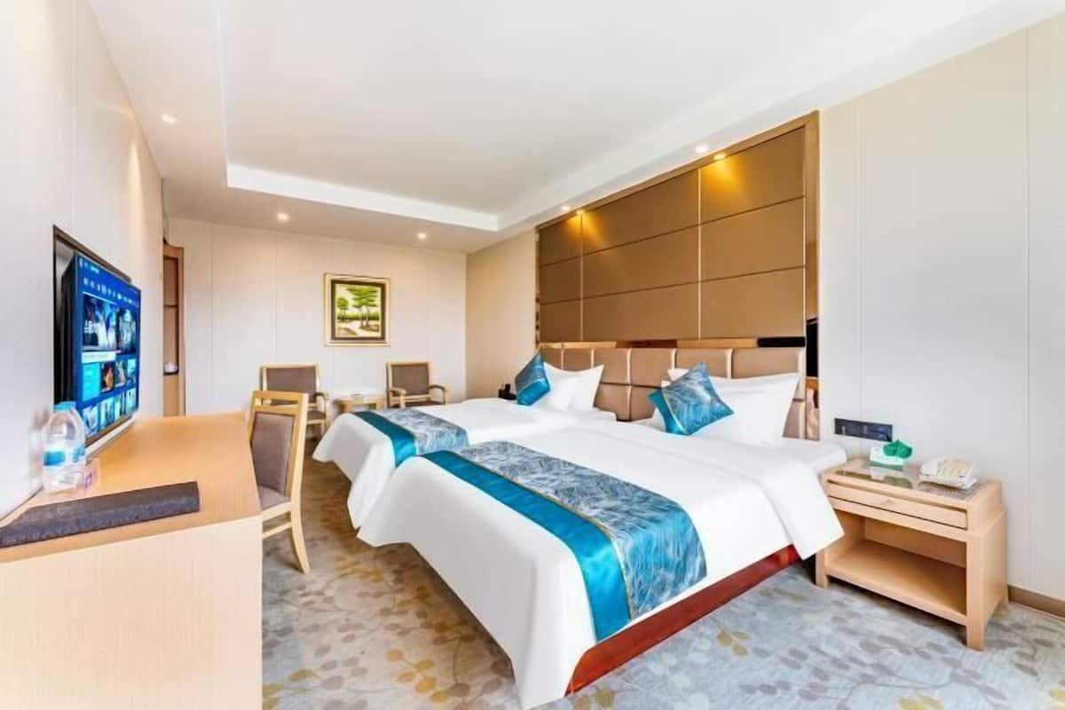 A hotel room with two beds, a desk, a TV, and a nightstand.
