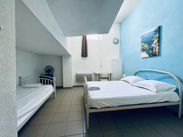 A room with two beds, a desk, a chair, a radiator, and a painting on the wall. - Balaena (Marseille)