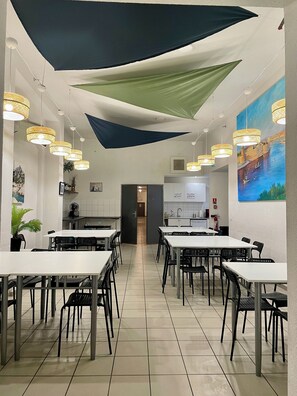 A spacious dining area with multiple tables and chairs, ceiling fans, and a large painting on the wall.