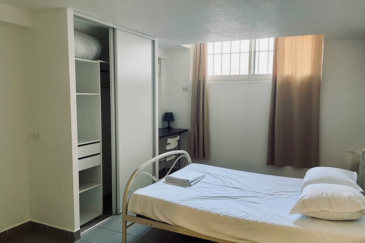 Une chambre à coucher avec un lit, une armoire, un bureau et une fenêtre avec des rideaux.