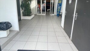 A building entrance with a tiled floor, a black mat with a white logo, a tree, and a sign for a sports aquatic center. - Balaena (Marseille)