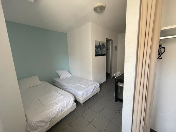 A room with two beds, a desk, and a door leading to another room.