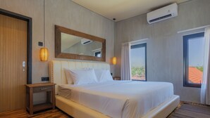 A hotel room with a large bed, a wooden nightstand, a mirror, an air conditioning unit, and a view of the outdoors through a window. - Ambhara X Apartment by Betterplace (Kerobokan)