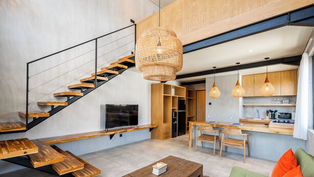 A modern living space with a wooden staircase, a dining area, and a kitchen. - Ambhara X Apartment by Betterplace (Kerobokan)