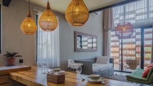 A modern kitchen with wooden countertops, a dining table set with plates and glasses, and wicker pendant lights. - Ambhara X Apartment by Betterplace (Kerobokan)