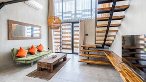 A modern living room with a green sofa, wooden coffee table, and a staircase with wooden steps. - Ambhara X Apartment by Betterplace (Kerobokan)