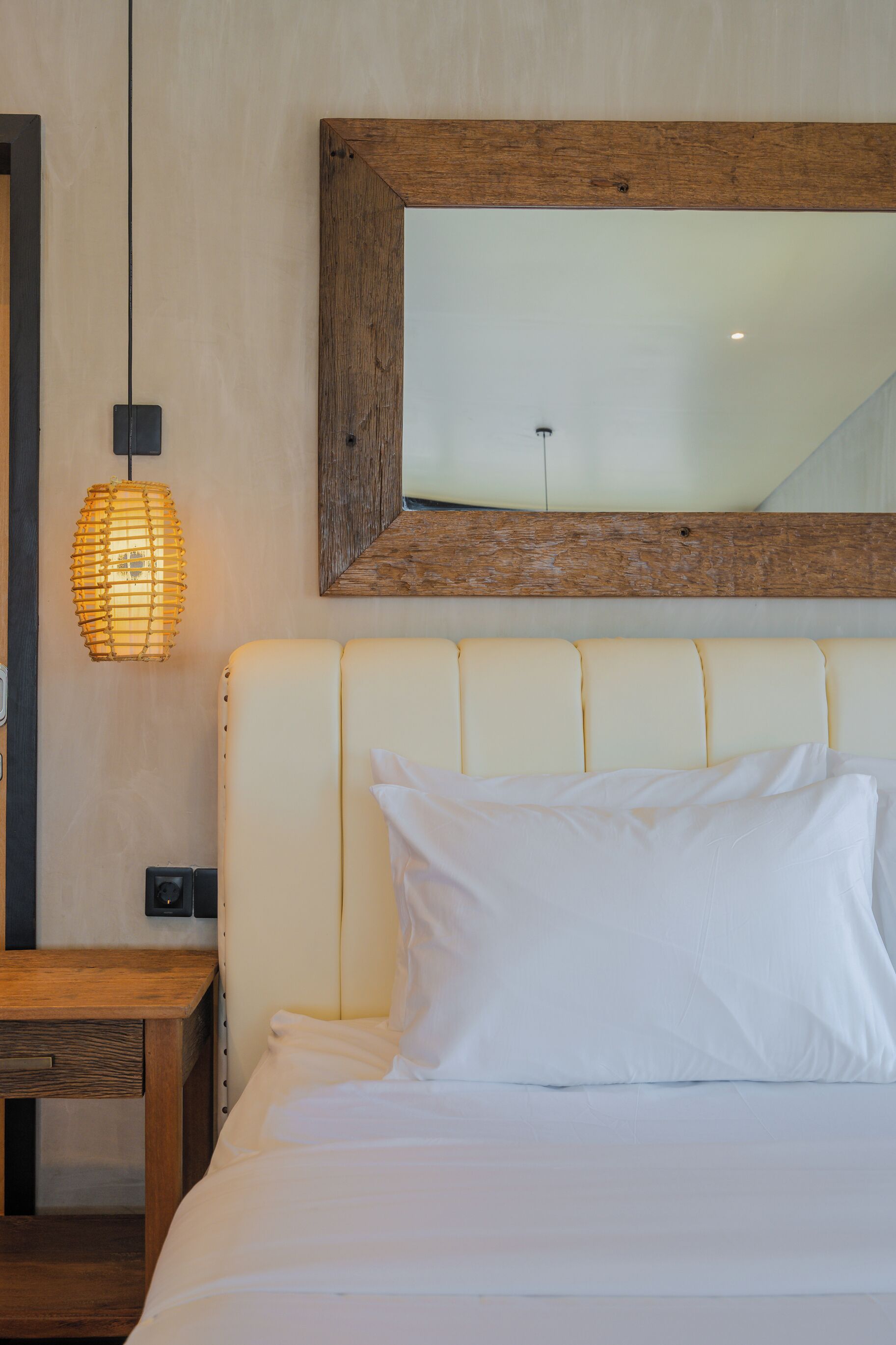 A bedroom with a large bed, a wooden headboard, a hanging light fixture, and a mirror above the bed.